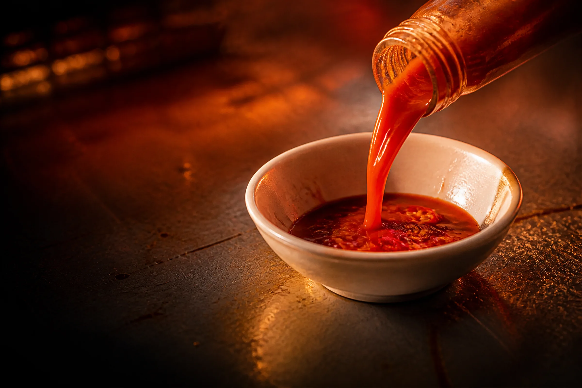 Sauce leaving the bottle and landing on the rim of a white bowl.