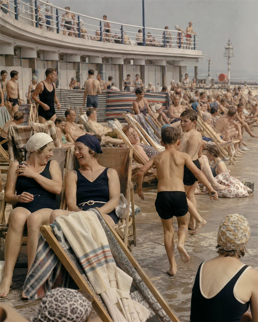 Swimmers and deck chairs crowded along the poolside on a hot afternoon.