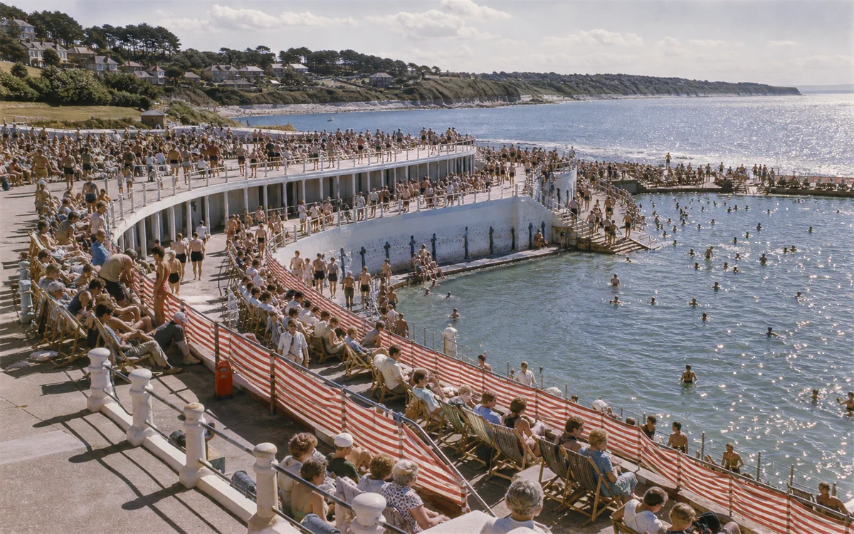 The curved seafront lido packed with swimmers and sunbathers, the sea beyond it.