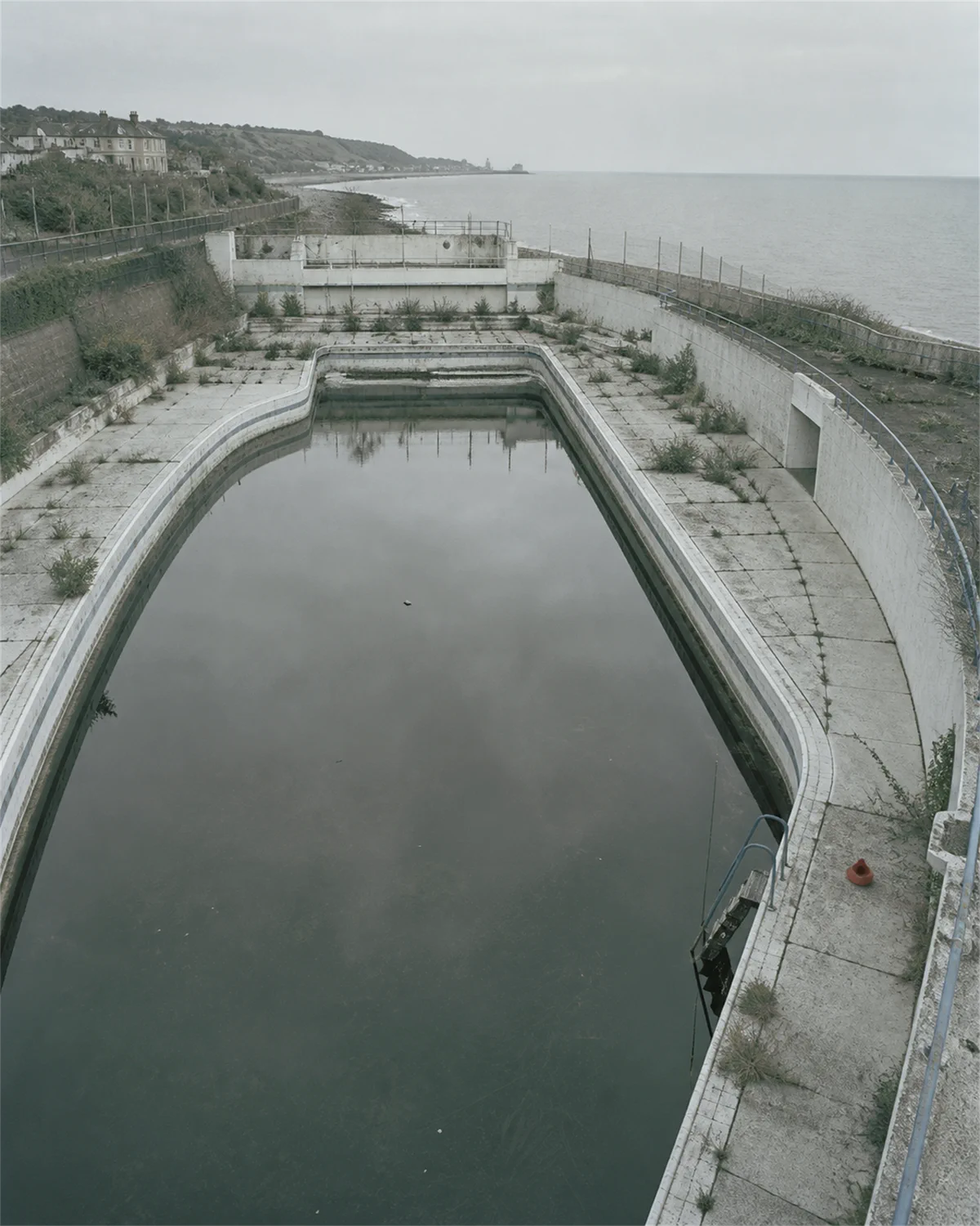 The empty basin holding still dark rainwater, seen from above with the coast behind.