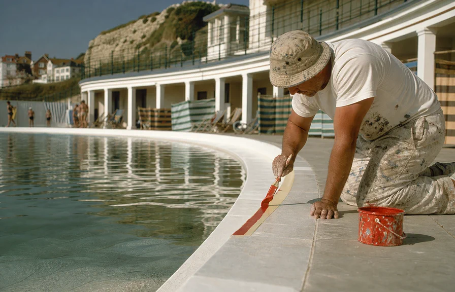 A painter cutting in the red stripe along the finished poolside.